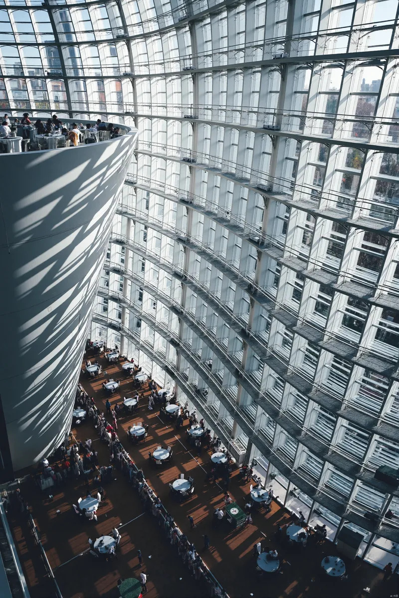 Interior view of a modern building showcasing curved glass windows and multiple floors with wooden flooring and white tables arranged inside