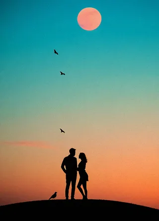 Silhouetted couple standing on a misty hilltop against a dreamy teal and pink sky, with a red-orange moon and birds flying in the background.
