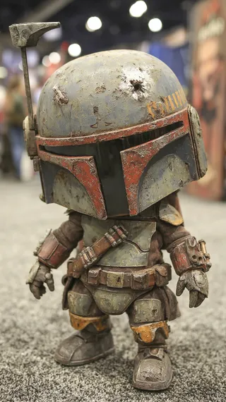 Miniature detailed figure of Boba Fett in worn armor and helmet, posed on a carpeted floor at a convention.