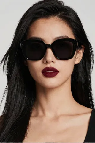 Close-up portrait of a woman with black hair wearing large black sunglasses, tanned skin, and dark red lips in a head photoshoot.