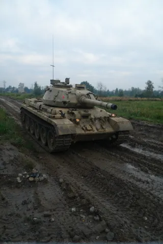 A Soviet tank driving over a muddy trench under a cloudy sky, viewed from a low angle in a battlefield setting.