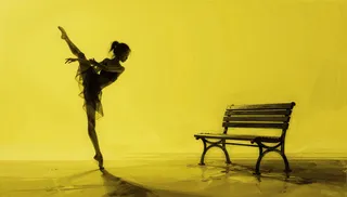 A graceful ballet dancer in black silhouette poses elegantly on one foot against a minimalistic yellow background, near a black park bench.