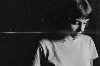High-contrast monochromatic film portrait of a young woman with a short bob hairstyle, wearing a light-colored t-shirt, illuminated by bright side light against a dark background with grain and film scratches.