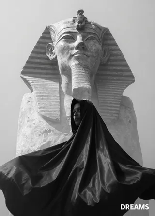Black-and-white image showing a large ancient Egyptian bust behind a dark cloaked figure partially visible through mist, with modern text 'DREAMS' in corner.