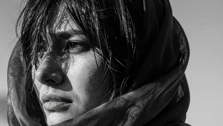 Close-up black and white portrait of a woman with wet black hair, furrowed brow, and slightly parted lips conveying melancholy, with chiaroscuro lighting and a translucent silk scarf partially covering her face.