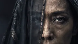 Close-up photorealistic portrait of a mature Bene Gesserit woman with intense gaze, stoic expression, partially obscured by dark grey-black fabric with metallic threading, lit with dramatic chiaroscuro lighting.