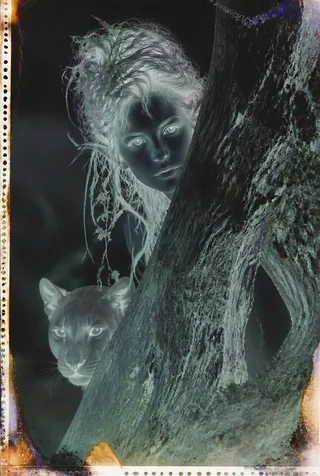 Photographic negative psychedelic portrait of a mysterious fae woman with elf ears, peering around a gnarled oak tree with her companion puma beside her.