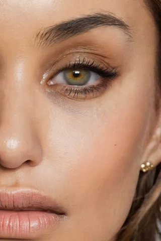 Close-up image of a woman's hazel eye showing detailed eyelashes, eye makeup, and natural facial skin texture.