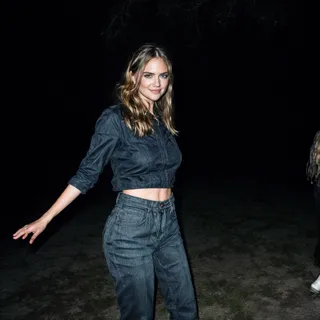 Smiling woman wearing a denim jacket and jeans in a night portrait taken with 90s flash photography style, hair gently flowing.