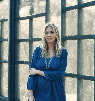 자연광이 스며드는 큰 창문 옆에 서 있는 파란 튜닉 드레스를 입은 흐르는 머리카락의 금발 여성