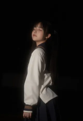 A young woman wearing a traditional black and white school uniform with black twintails, eyes closed, softly lit against a black background.