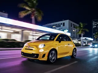 Yellow Fiat 500 car driving quickly through a Miami city street at night with motion blur, neon lights, and palm trees.