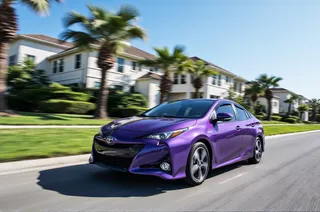 Purple Toyota Prius speeding on a residential street with palm trees and mansions, motion blur effect with clear blue sky in background.
