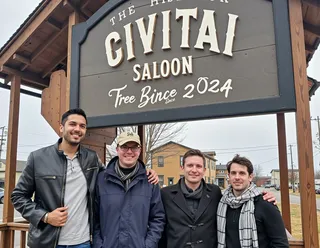 Four men standing together in winter clothing under a large wooden sign reading 'Civitai Saloon Free Buzz Since 2024' in a foggy historic town setting.