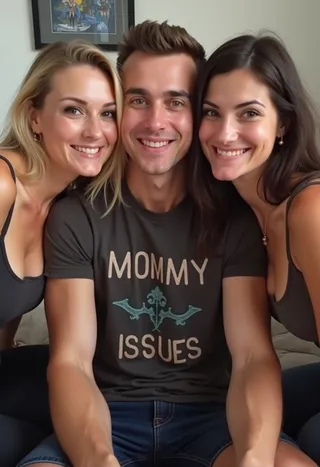 A handsome young man wearing a 'Mommy Issues' shirt sitting smiling between two women in tank tops indoors.