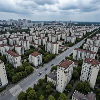 Wide angle drone footage showing rows of Soviet-era apartment buildings in a sprawling city with tree-lined streets under a cloudy sky.