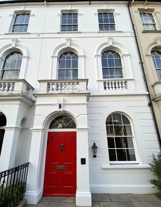 Luxury British townhouse with four stories, featuring a bright red door, white walls, arched windows with balustrades, captured in detailed architectural photography.