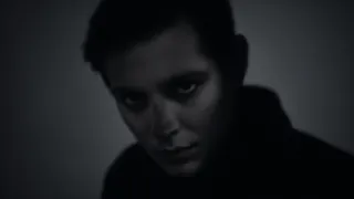 A dark, ghostly portrait in chiaroscuro style showing a person's face partially obscured by dramatic shadows and moody lighting.