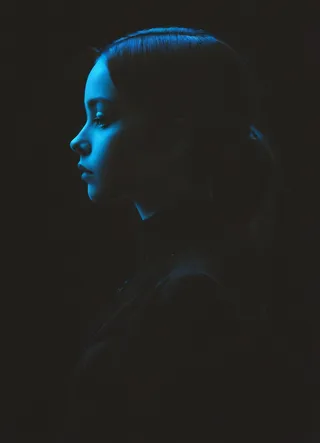 Silhouette profile portrait of a woman in low-key lighting with blue illumination on her face, set against a dark background.