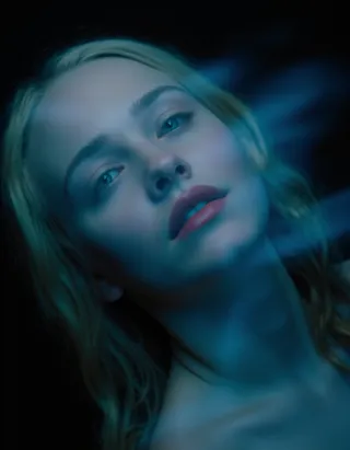 Blurry portrait of a woman with blonde hair and red lips illuminated in blue light against a black background with motion blur effect.