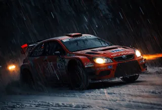 Red rally car racing through a snowy forest at night with heavy snow and glowing warm headlights.