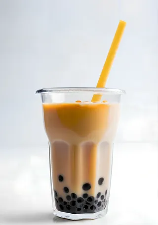 Cold condensed milk flavored boba tea in a clear plastic cup with a yellow straw and black tapioca pearls at the bottom, set against a white background.