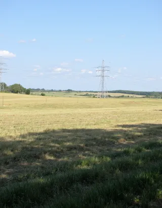 Open grassy field under a clear blue sky with metal transmission line towers and power lines stretching across the landscape