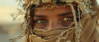 Close-up of a desert princess's face with sun-scorched skin, piercing amber eyes, beaded veil, windblown hair, and ancient headpiece in a dusty desert environment.