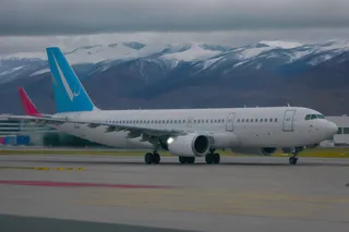 High quality photo of an Airbus A321 airplane taking off on a rainy, cloudy day at an airport with snowy mountains in the background.