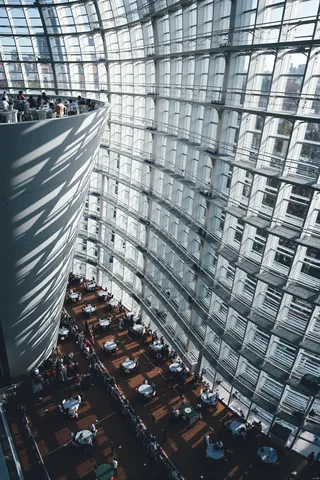 Top-down view of an interior featuring a curved glass window wall, natural light illuminating dark brown wooden floors with white tables and chairs arranged in a semi-circle pattern.
