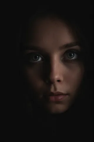 Close-up portrait of a woman's face with intense eye focus, cozy lighting, and a dark background emphasizing negative space.