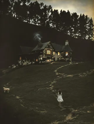 Colorized old photograph of an antique cottage on a hill in the Pyrenees foothills at twilight, showing warmly lit windows, smoke rising from the chimney, and a young shepherdess walking uphill.