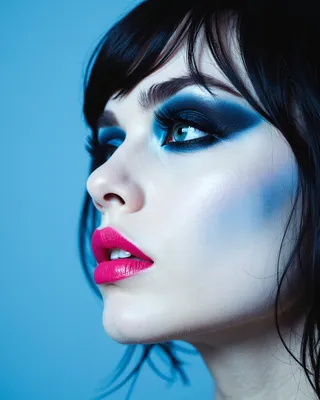 Close-up forced perspective profile of a goth woman wearing a sky blue beret, with pale skin, dramatic blue eye makeup, and vibrant pink glossy lips.
