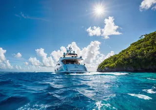 Luxury yacht sailing through vibrant blue Caribbean waters near a lush green island under bright sun rays and a dramatic sky.