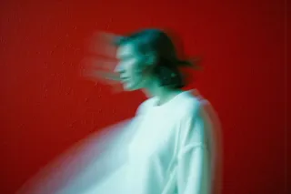 Blurred image of a person wearing a white shirt standing sideways against a vivid red textured wall background, showcasing motion blur effect.
