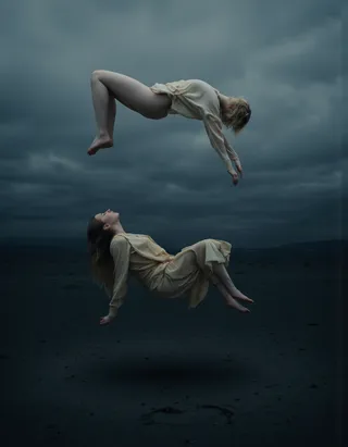 A surreal portrait of two women in flowing gowns levitating above a dark, desolate landscape under a cloudy sky, conveying weightlessness and mystery.