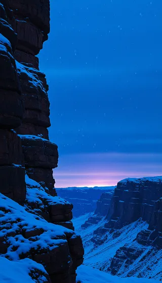 Snow-covered rock cliffs under a deep blue sky with snowflakes gently falling at sunset, revealing a desert canyon landscape in low saturation tones.