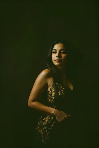 Portrait of a Mexican woman in a dark setting, softly illuminated with detailed gold embroidery on her dress, captured in a photographic style.