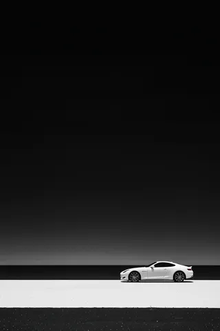 High contrast black and white image of a sleek white sports car positioned on a minimalist road against a serene dark sky background.