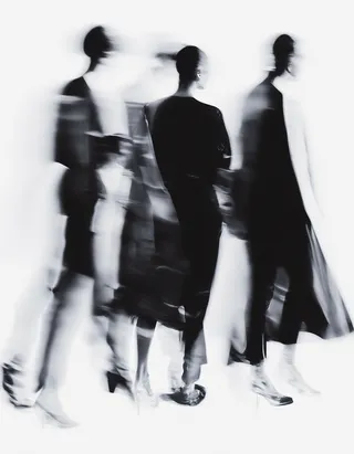 Blurred black and white abstract image featuring four individuals in minimalist dark clothing with selective focus details, set against a white background.