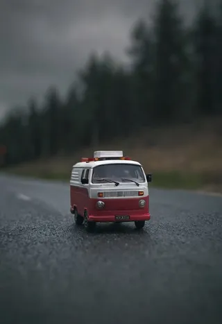 Macro shot of a red and white toy van on a road with a dark moody atmosphere and gradual blur effect creating an aesthetic mood.