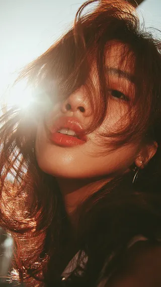 髪を日の光が照らし、輝く肌と自然なメイクでやや開いた唇の女性のクローズアップポートレート。