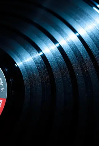 Close-up of a vinyl record surface reflecting cinematic blue light with visible grooves and film grain texture.