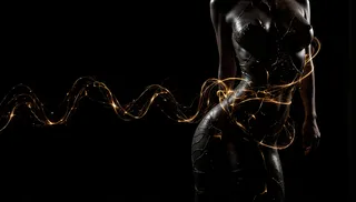 Silhouette of a female body in a sexy dress with glowing, flowing light strands and abstract particles against a black background.