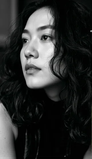 Black and white portrait of a woman with long wavy hair, shown in profile, with soft natural lighting highlighting her calm, elegant expression.