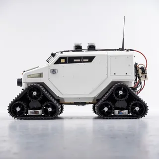 Side view of a futuristic armored vehicle with white exterior, large black tracked treads, industrial design, and mounted sensors on top.