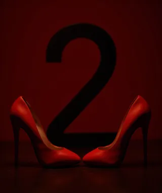 Red high heels facing each other with a large black number 2 in the background on a dark red backdrop
