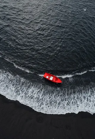 Top view drone photo of a red boat on black sea water with white waves rolling toward a black sand beach in minimalist style.