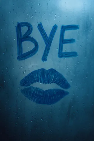 Close-up of a foggy window with blue lipstick drawing spelling 'BYE' and a kiss print below, with water droplets and ambient haze.