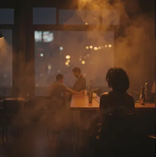 Silhouette of a woman with curly hair wearing a black dress sitting alone at a dimly lit bar counter filled with smoke, with two blurred figures in the background and warm spotlights shining through.
